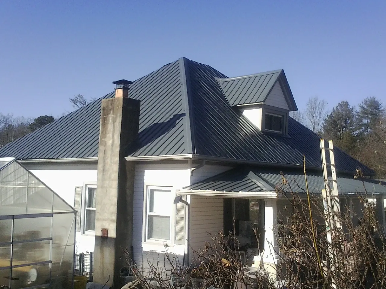 Dark blue standing seam metal roof on a white farmhouse with dormer — Slate & Tile Roof Repair by Roofing Brothers in Nassau