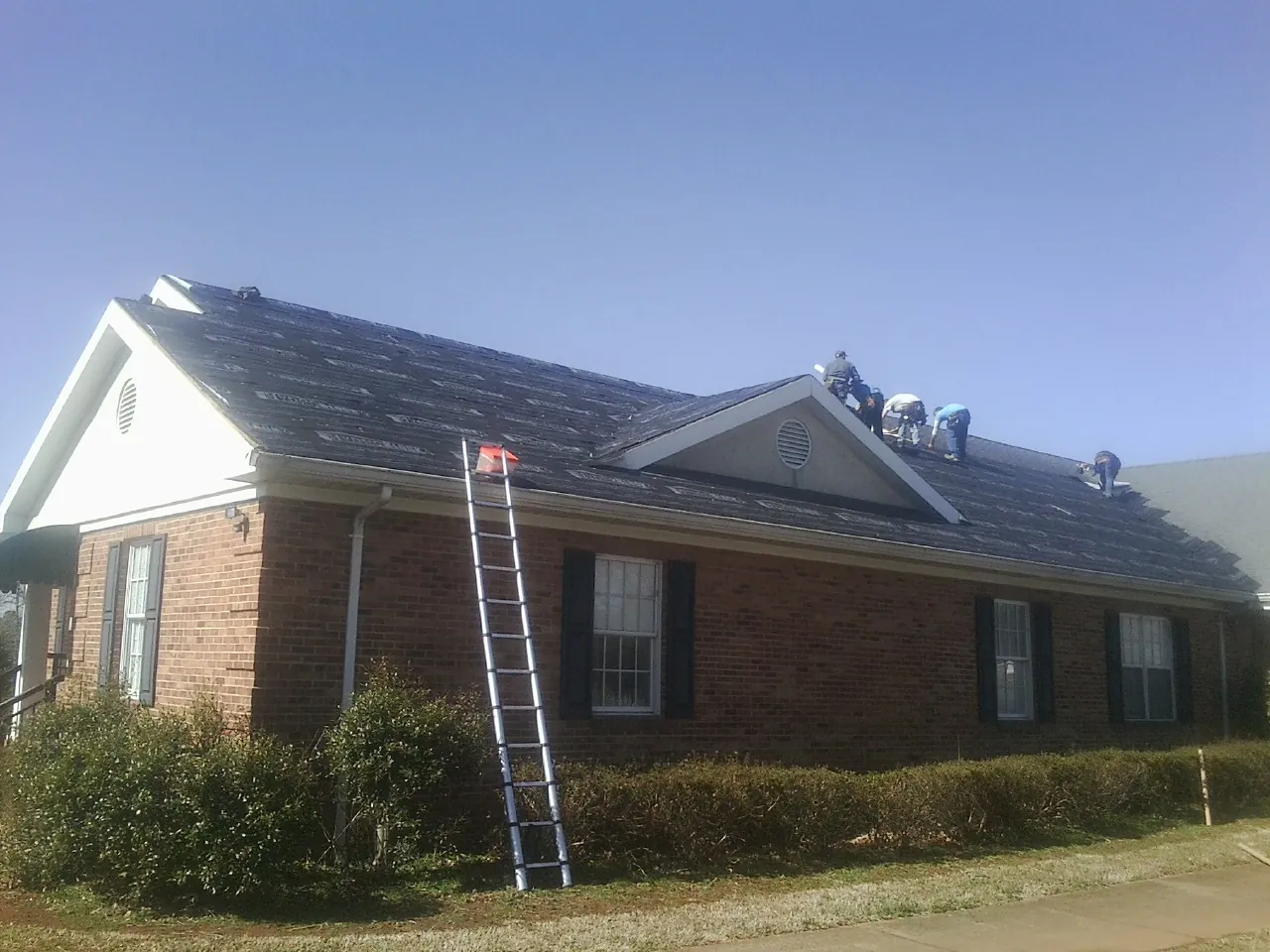 Crew tearing shingles off a brick ranch roof with a ladder set — Metal Roof Repair work by our crew in Nassau