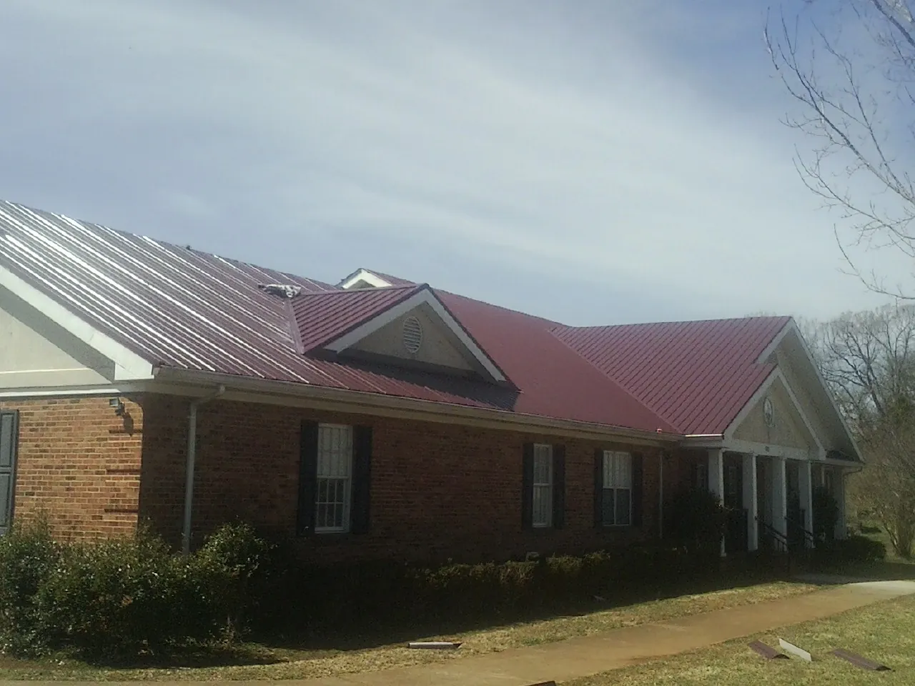 Red metal roof with gabled entries on a long brick building, from a Hail Damage Roof Repair job in Nassau