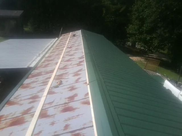 Old rusted panels beside newly installed green metal roofing — Wind Damage Roof Repair by Roofing Brothers in Nassau