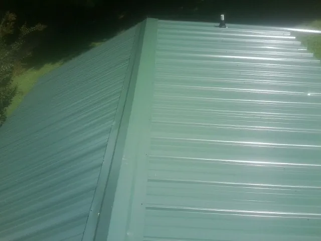 New green metal panels meeting at the ridge of a roof — Flat Roof Repair work by our crew in Nassau