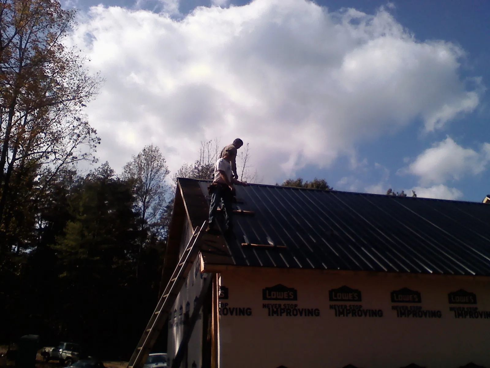 Roofer fastening dark metal panels high against a cloudy sky, from a Roof Inspection job in Nassau