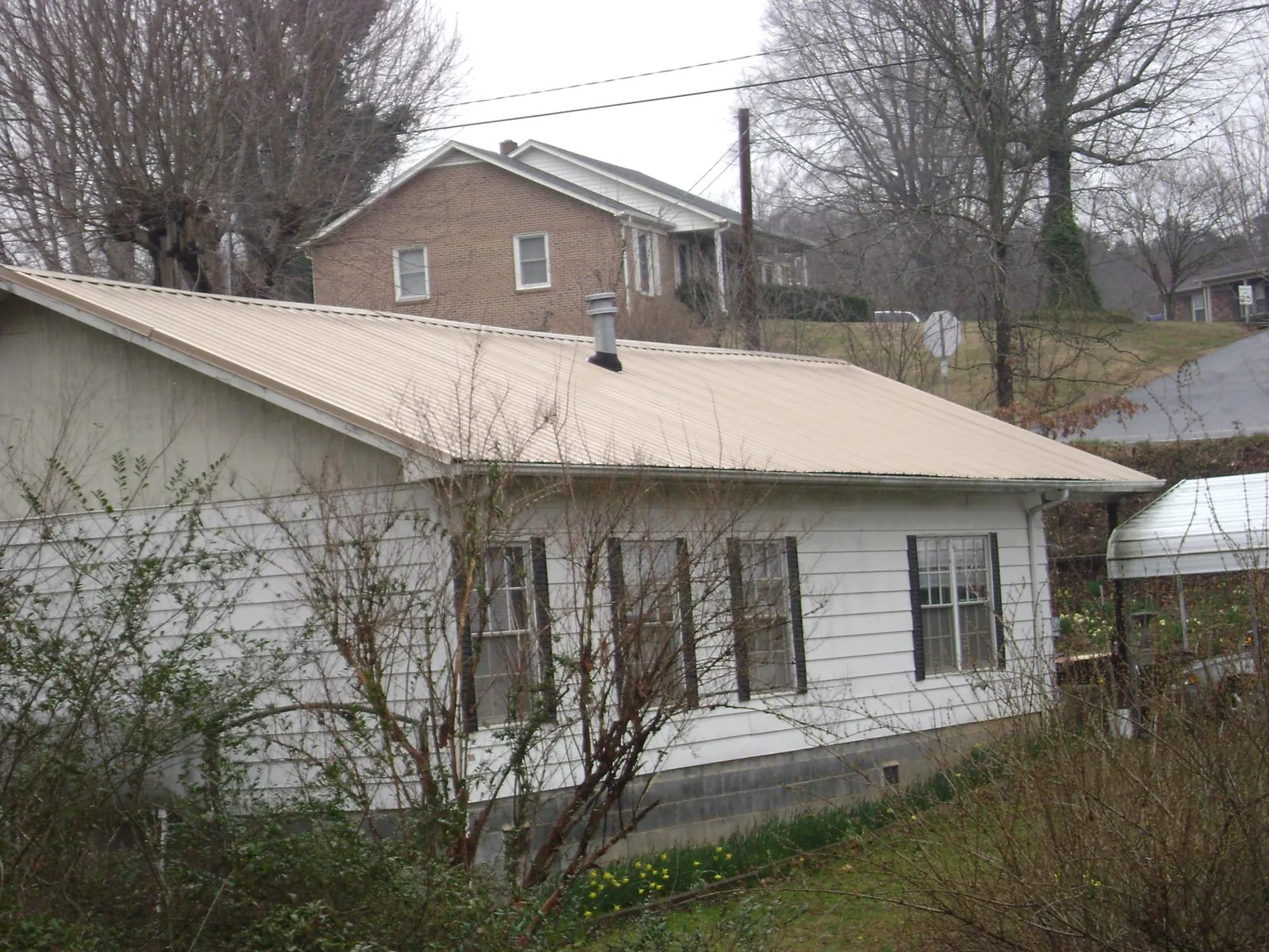 Tan metal roof on a white sided house set into a hillside — Commercial Roofing by Roofing Brothers in Nassau