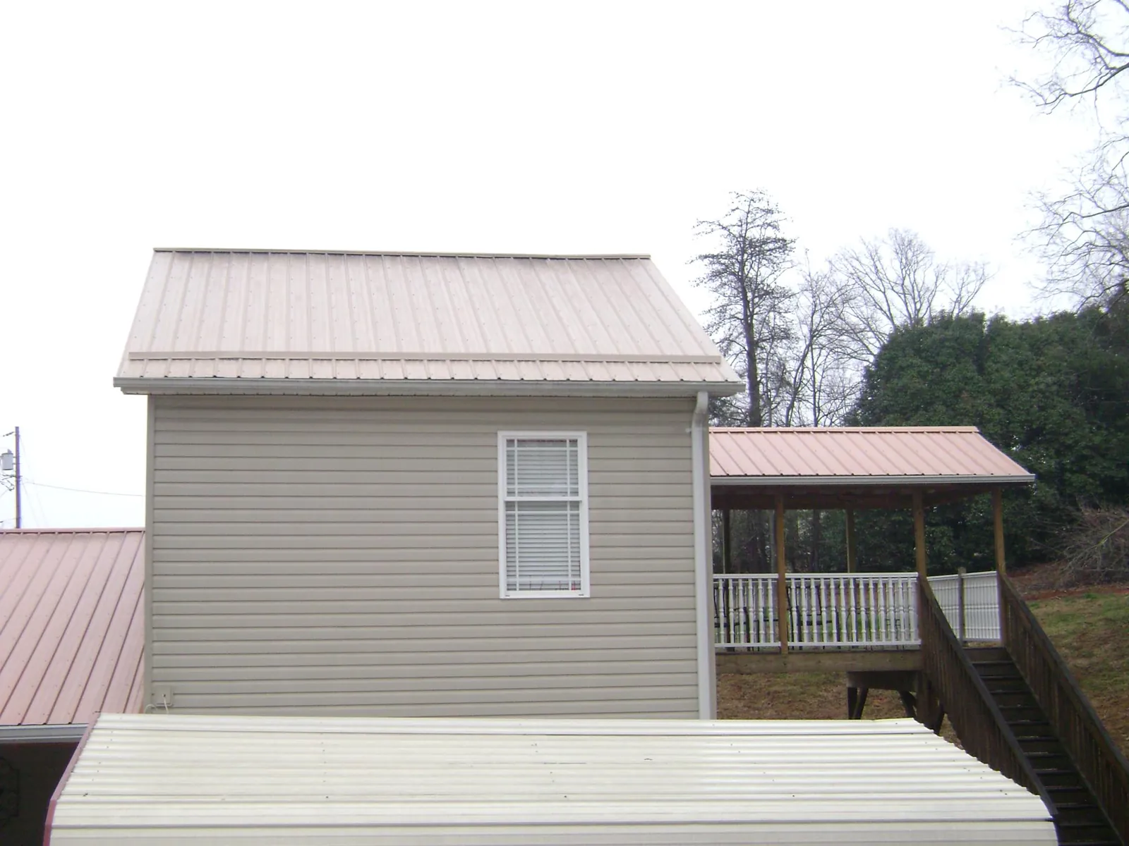 Tan metal roofs on a two story addition and attached porch, from a Roof Replacement job in Nassau